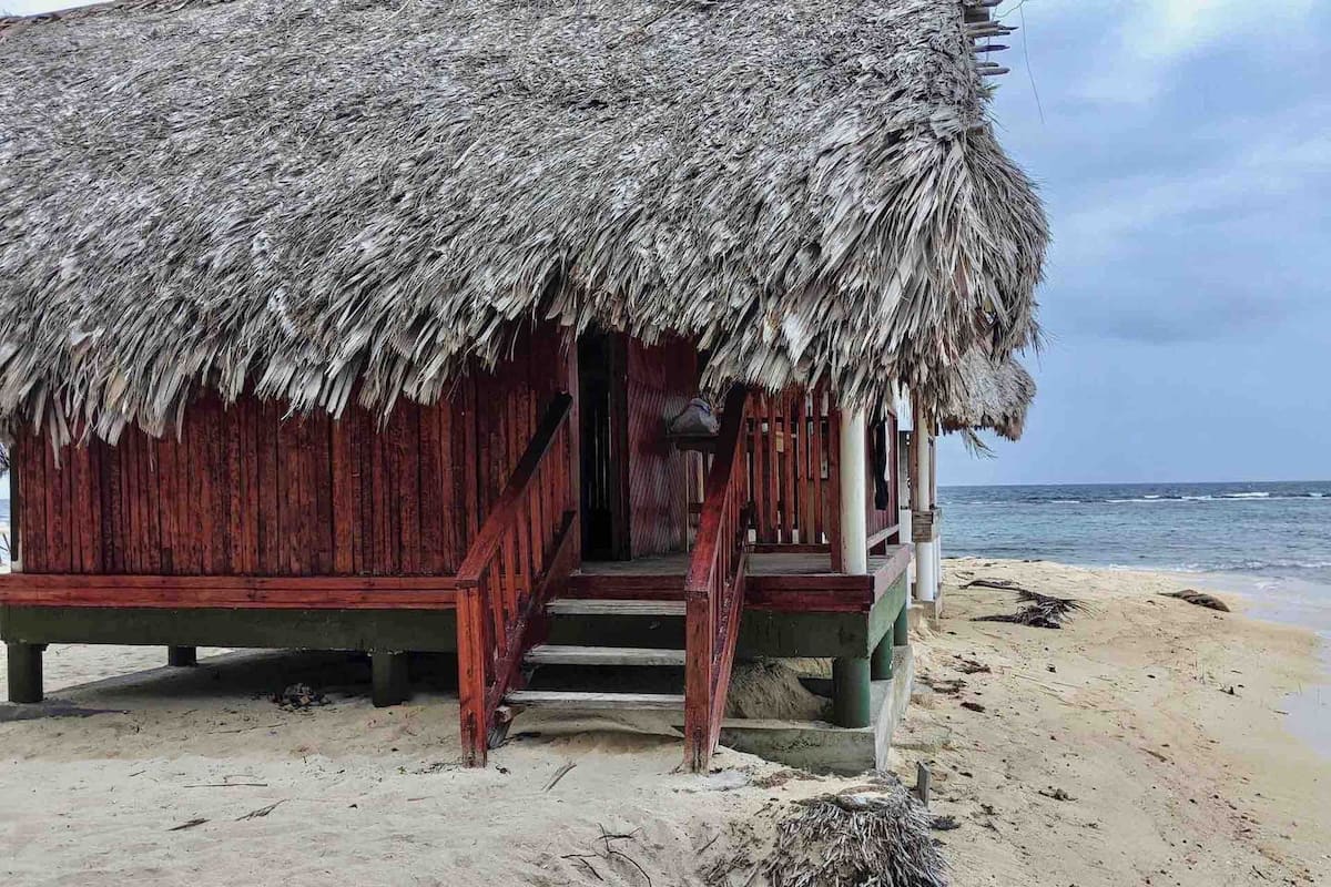 Uma cabana de madeira com telhado de palha numa praia de areia.