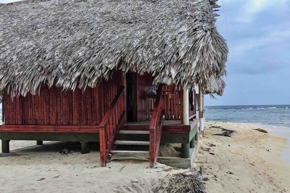 Eine Holzhütte mit einem Reetdach am Sandstrand.