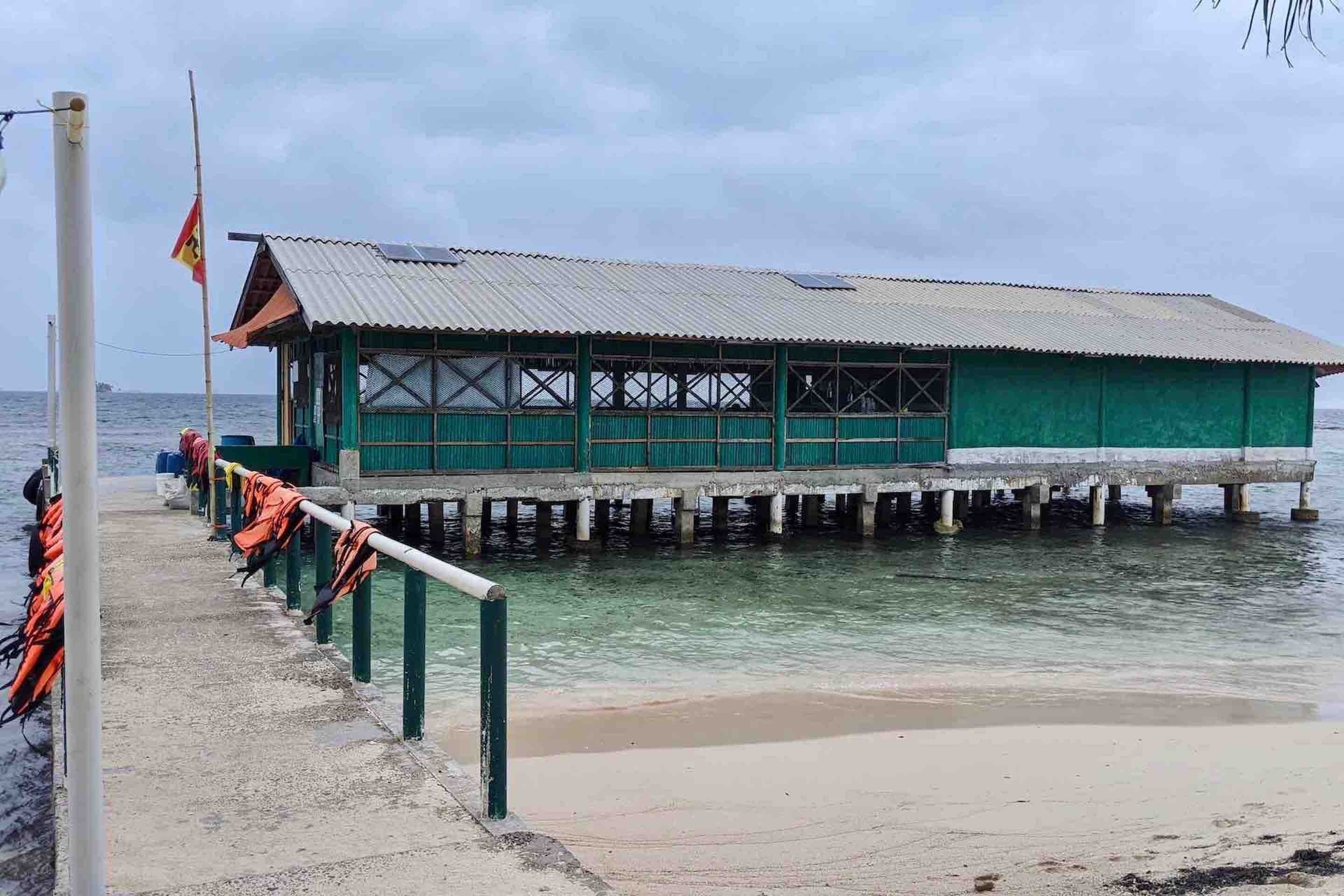 A green building with a metal roof, located on stilts over water.