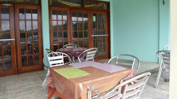 A dining area with a table and chairs, a fan, and a view through a glass door. - Tapion Beach Suites 1 (Castries)