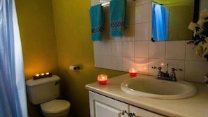 A bathroom with a toilet, sink, and mirror. There are towels hanging on the wall and candles on the sink. - Tapion Beach Suites 1 (Castries)