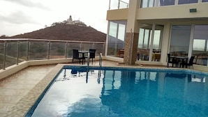 Una piscina en la azotea con vistas despejadas a una colina y un edificio a lo lejos.