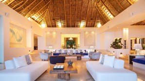 A spacious lobby with a high thatched ceiling, a central seating area with sofas and a coffee table, and a staircase leading to upper floors.