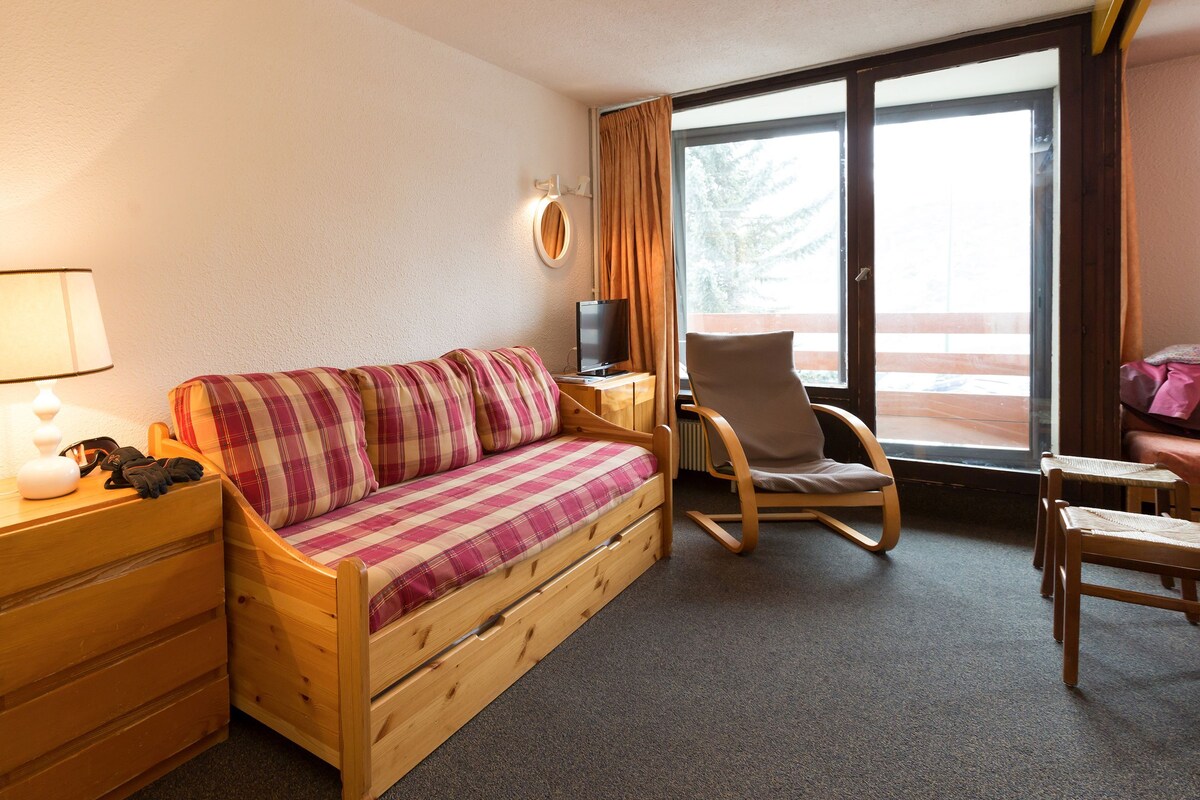 A cozy room with a wooden bed, a chair, a small table, a lamp, and a TV.