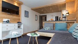 A modern room with a sofa, a small table, a TV, and a wooden ceiling. - Résidence Odalys Chanteneige Croisette (Les Belleville)