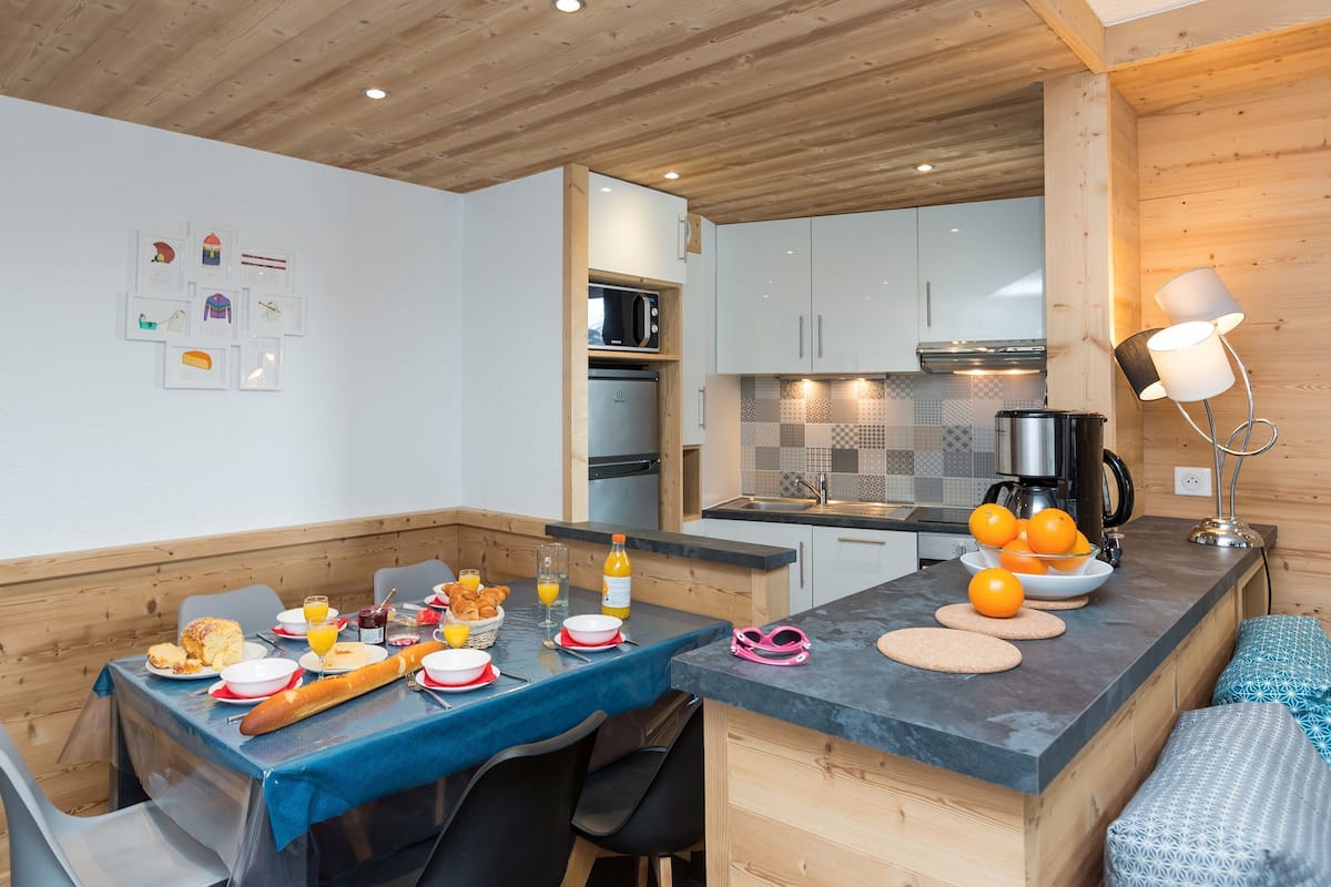 A modern kitchen with wooden cabinets, a dining area with a blue tablecloth, and a breakfast setting.