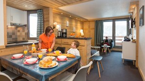 A dining area with a table set for breakfast, including croissants, bread, and orange juice. - Résidence Odalys Chanteneige Croisette (Les Belleville)