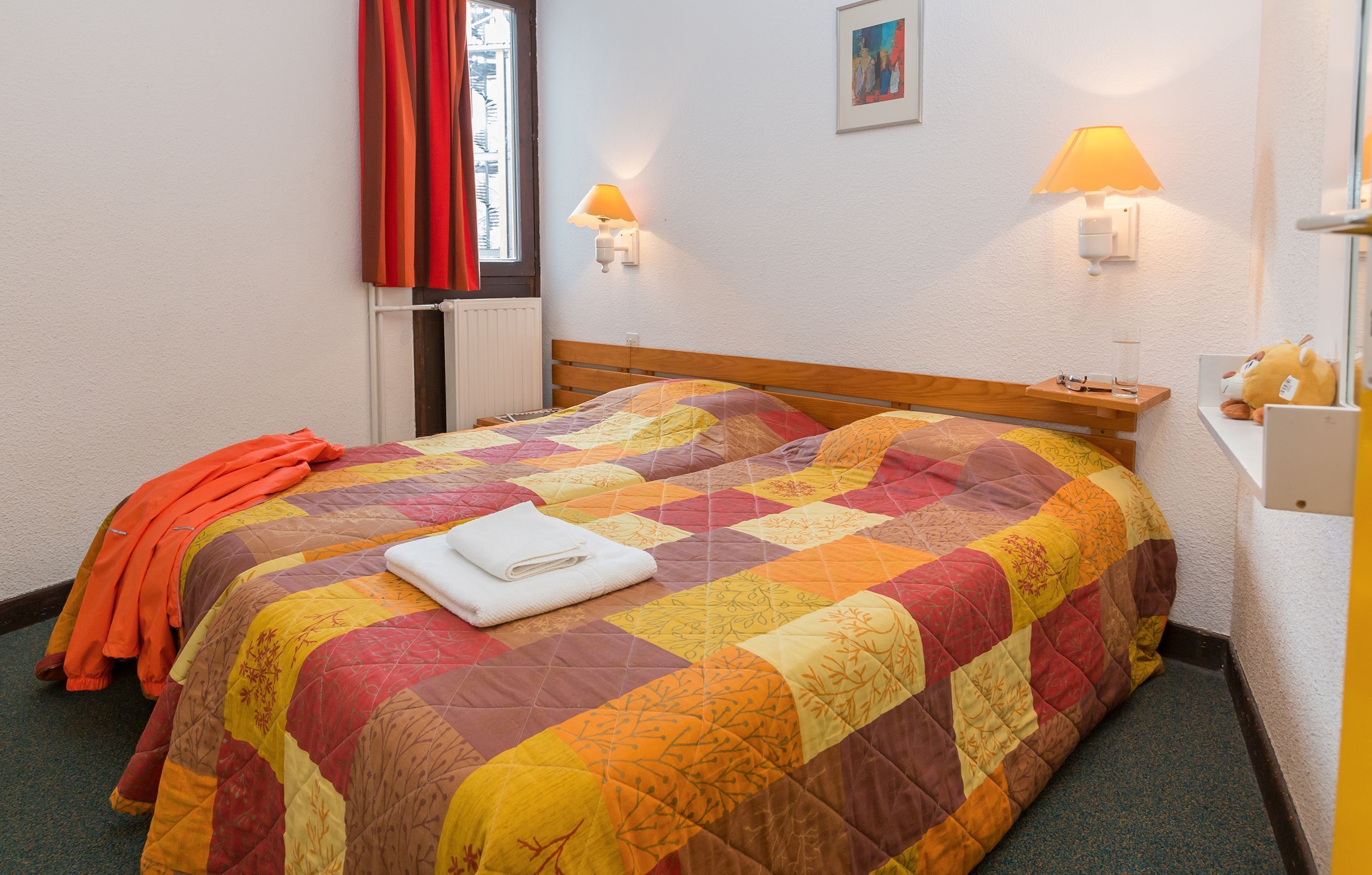 A bed with a quilt, a nightstand, a lamp, and a window with curtains.