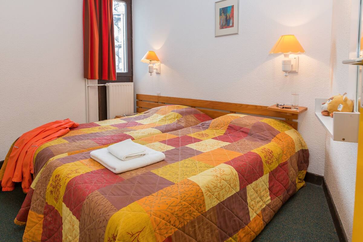 A bed with a quilt, a nightstand, a lamp, and a window with curtains.
