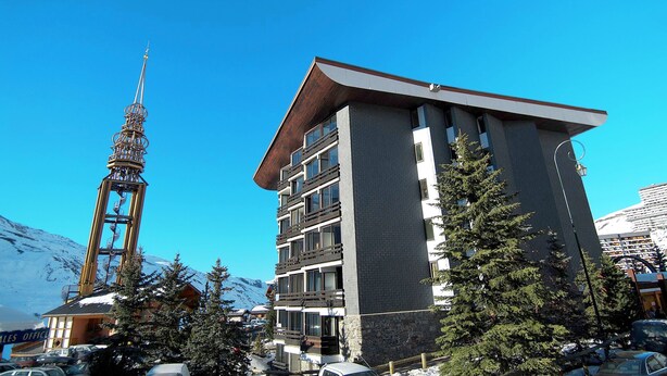 A multi-story building with balconies and large windows, surrounded by snow-capped mountains and a clear blue sky. - Résidence Odalys Chanteneige Croisette (Les Belleville)