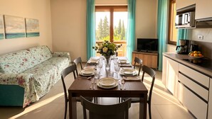 Comedor con una mesa para cuatro, un sofá, un televisor y una zona de cocina con microondas.