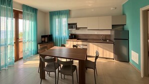 Una cocina moderna con comedor, televisor y balcón con cortinas.