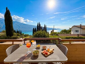 A table with a view of mountains and a lake, a glass of orange juice, a bowl of olives, and a plate with cheese and ham. - Appartamento 205 Benaco (Tignale)