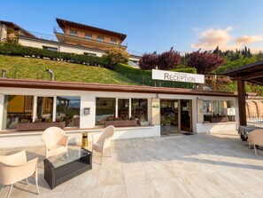 A reception area with outdoor seating, a signboard, and a building in the background. - Appartamento 205 Benaco (Tignale)
