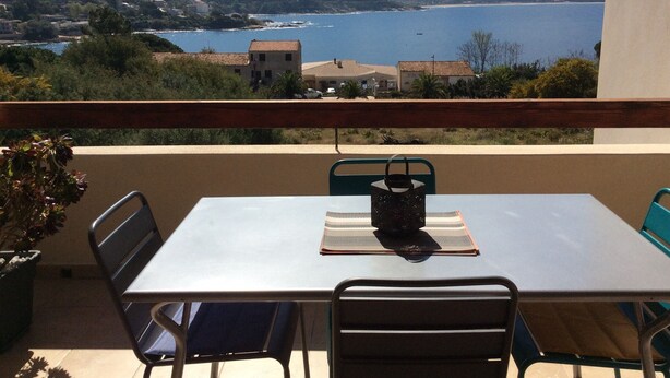 Un balcón con mesa y sillas, con vista al litoral, montañas y una masa de agua.