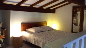 Un dormitorio con techo de madera, una cama con colcha blanca, dos lámparas de noche y un mesita de noche de madera.
