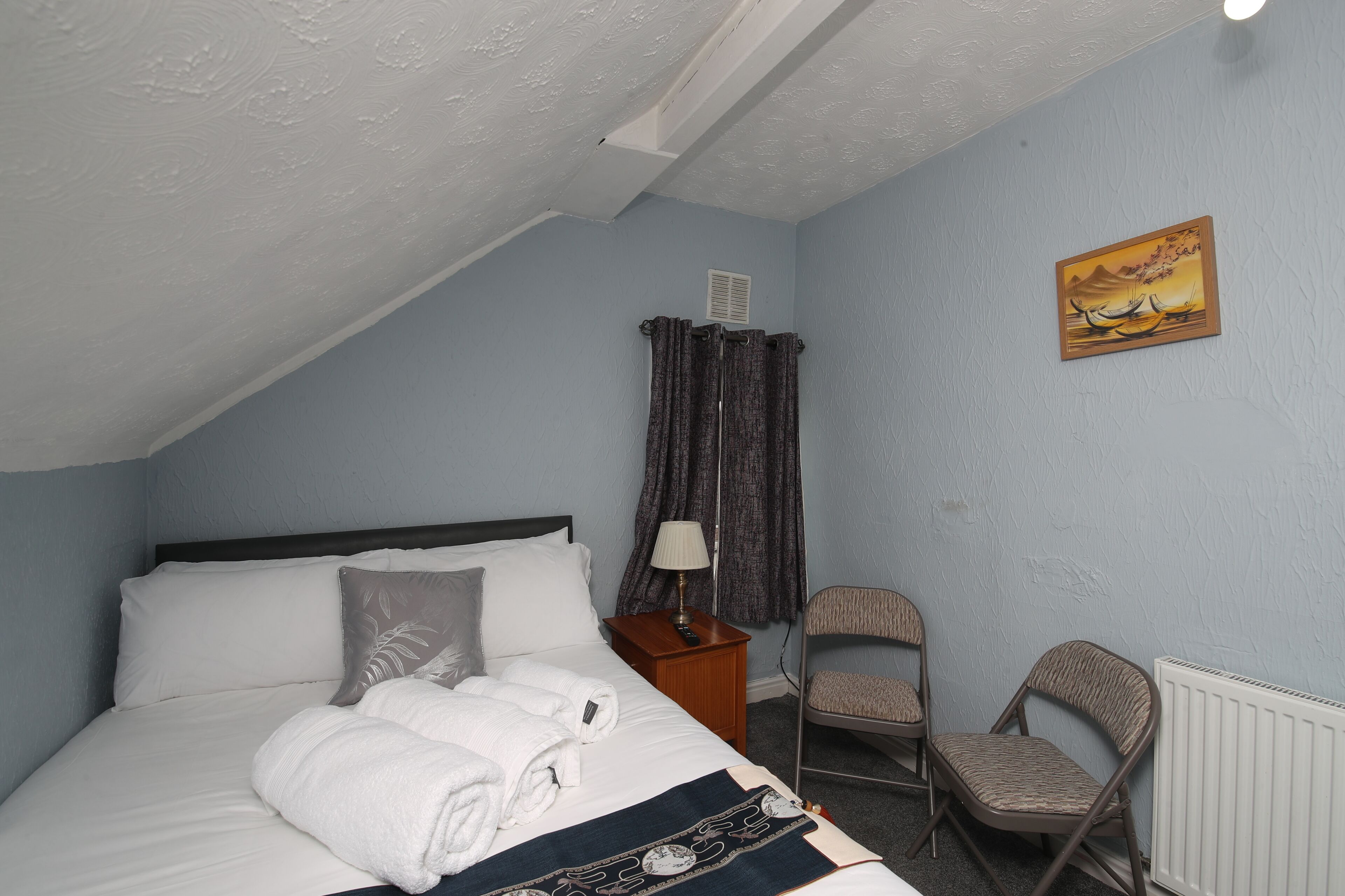A bedroom with a bed, a chair, a nightstand, a lamp, and a painting on the wall.