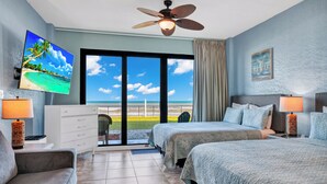 A hotel room with a bed, a TV, a ceiling fan, a desk, a chair, and a view of the beach. - First Floor Private Paradise Ocean Front Studio SPRING SALE! POOL OPEN!! (Daytona Beach)