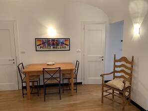 A dining area with a wooden table and chairs, a framed artwork on the wall, and a door with a light fixture. - Cassa di Loggia Sleeps 4 With Pool (Castelbianco)