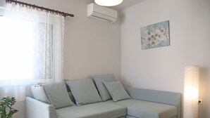 Un salon avec un canapé bleu clair, une petite table, une plante en pot et un climatiseur fixé au mur.
