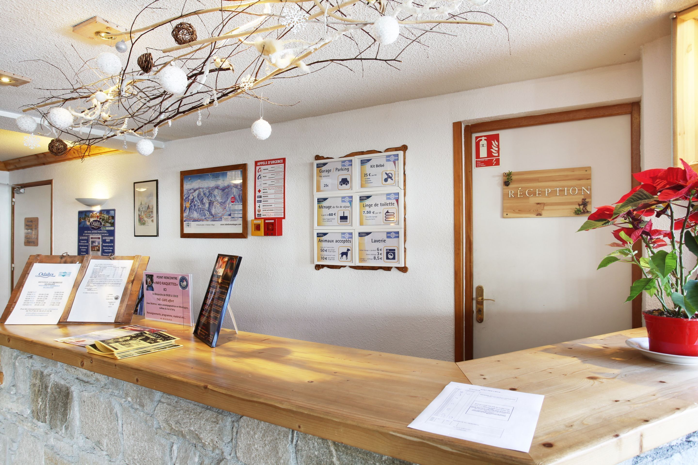 Un comptoir d’accueil avec des affiches d’information, un panneau indiquant les consignes de sécurité incendie et un panneau en bois signalant la zone d’accueil.