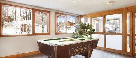 A pool table in a room with large windows and a view of a snowy mountain.