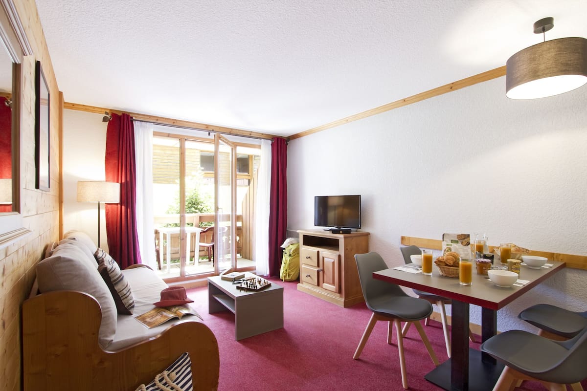 A cozy living room with a sofa, coffee table, TV, and dining area with chairs and a table set for breakfast.