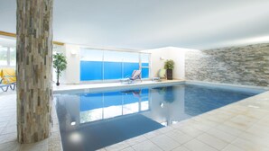 Une piscine intérieure à l’eau d’un bleu cristallin, avec un pilier en pierre et une vue sur l’océan grâce à de grandes fenêtres.