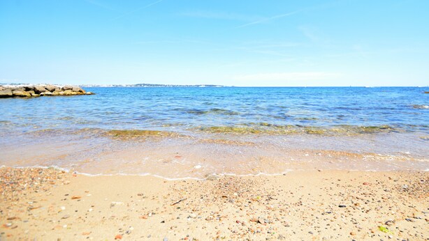 A beach with clear blue water, pebbles, and a rocky breakwater. - Cannes Eden. Large sea view studio, beach access, quiet, swimming pool and tennis. (Vallauris)