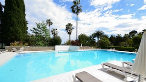 A swimming pool with lounge chairs and a stone wall. - Cannes Eden. Large sea view studio, beach access, quiet, swimming pool and tennis. (Vallauris)