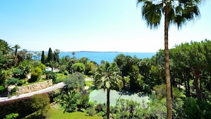 A tennis court surrounded by lush greenery and a stone wall. - Cannes Eden. Large sea view studio, beach access, quiet, swimming pool and tennis. (Vallauris)