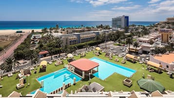 Relax by the resort's rectangular pool surrounded by lush lawns and lounge chairs, with the ocean visible in the distance.