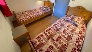 Una habitación pequeña con dos camas individuales, cada una con ropa de cama estampada. Hay una pequeña mesa de madera y una lámpara fijada a la pared.