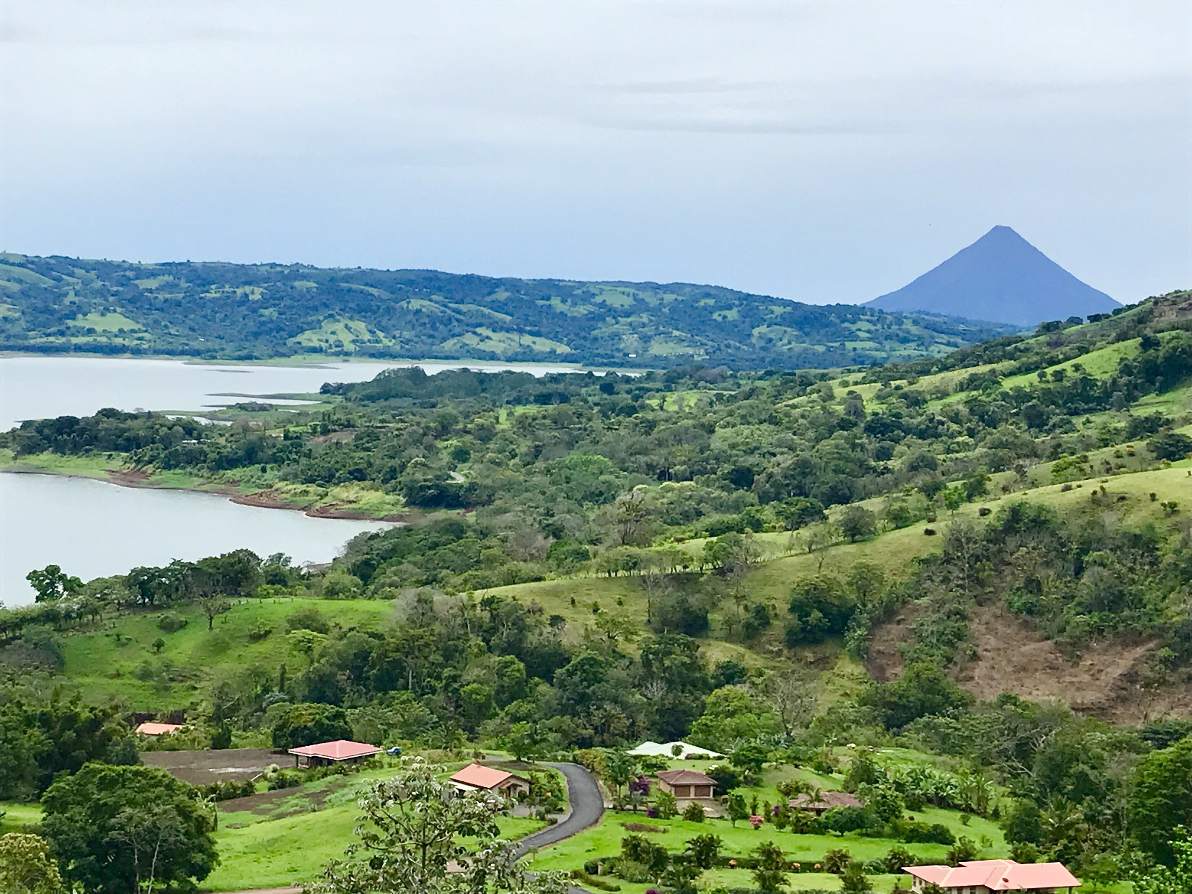 Un paisaje verde y exuberante con un lago, colinas ondulantes y una montaña destacada al fondo.