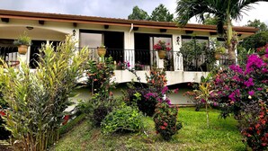A building with a balcony, surrounded by various plants and flowers. - Stunning views of Lake Arenal & Volcano in Secure Safe Gated Vacation Community (Tronadora)