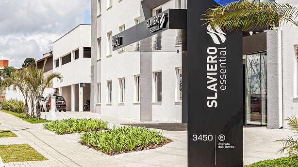 A hotel sign with "HOTEL" and "SLAVIERO essential" branding, a modern building facade, and a paved pathway with greenery. - SLAVIERO Curitiba Aeroporto (Sao Jose dos Pinhais)