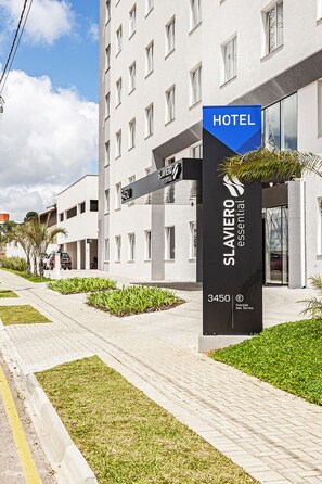 A hotel sign with "HOTEL" and "SLAVIERO essential" branding, a modern building facade, and a paved pathway with greenery. - SLAVIERO Curitiba Aeroporto (Sao Jose dos Pinhais)