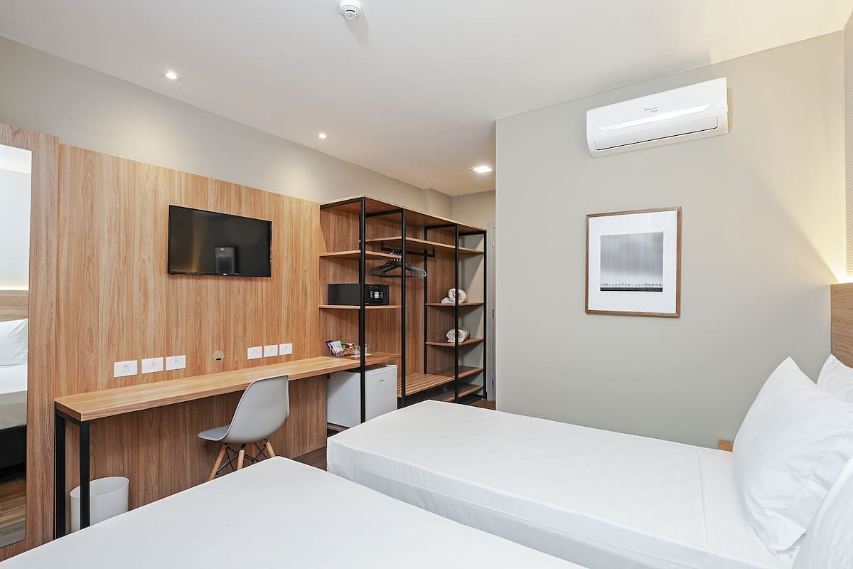 Ein Hotelzimmer mit Bett, Schreibtisch mit Stuhl, Fernseher, Kleiderschrank und kleinem Kühlschrank.