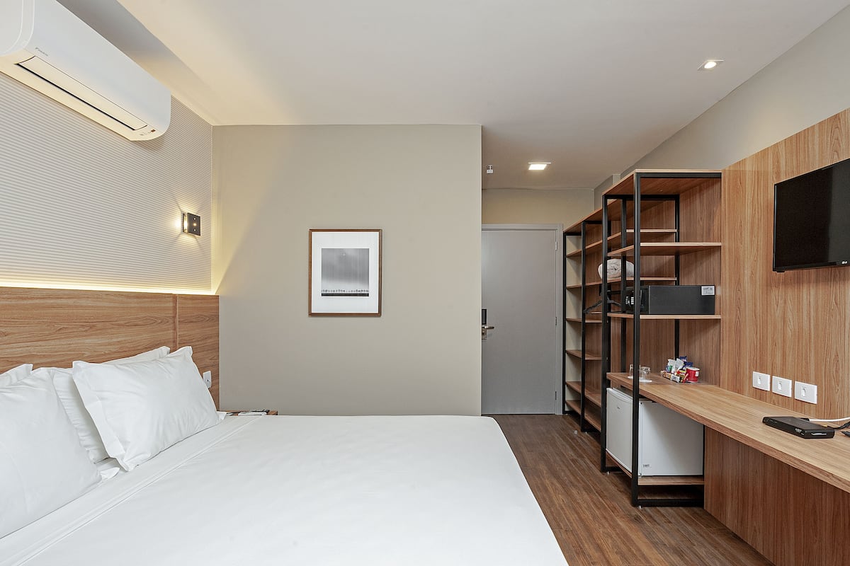 Ein Hotelzimmer mit Bett, Schreibtisch, Flachbildfernseher, integrierten Regalen und einem gerahmten Bild an der Wand.