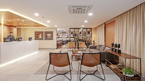 A modern hotel lobby with a reception desk, seating area, and a coffee station. - SLAVIERO Curitiba Aeroporto (Sao Jose dos Pinhais)