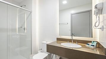 Un baño moderno con ducha de vidrio, inodoro blanco, lavamanos con encimera color beige y un secador de pelo montado en la pared.