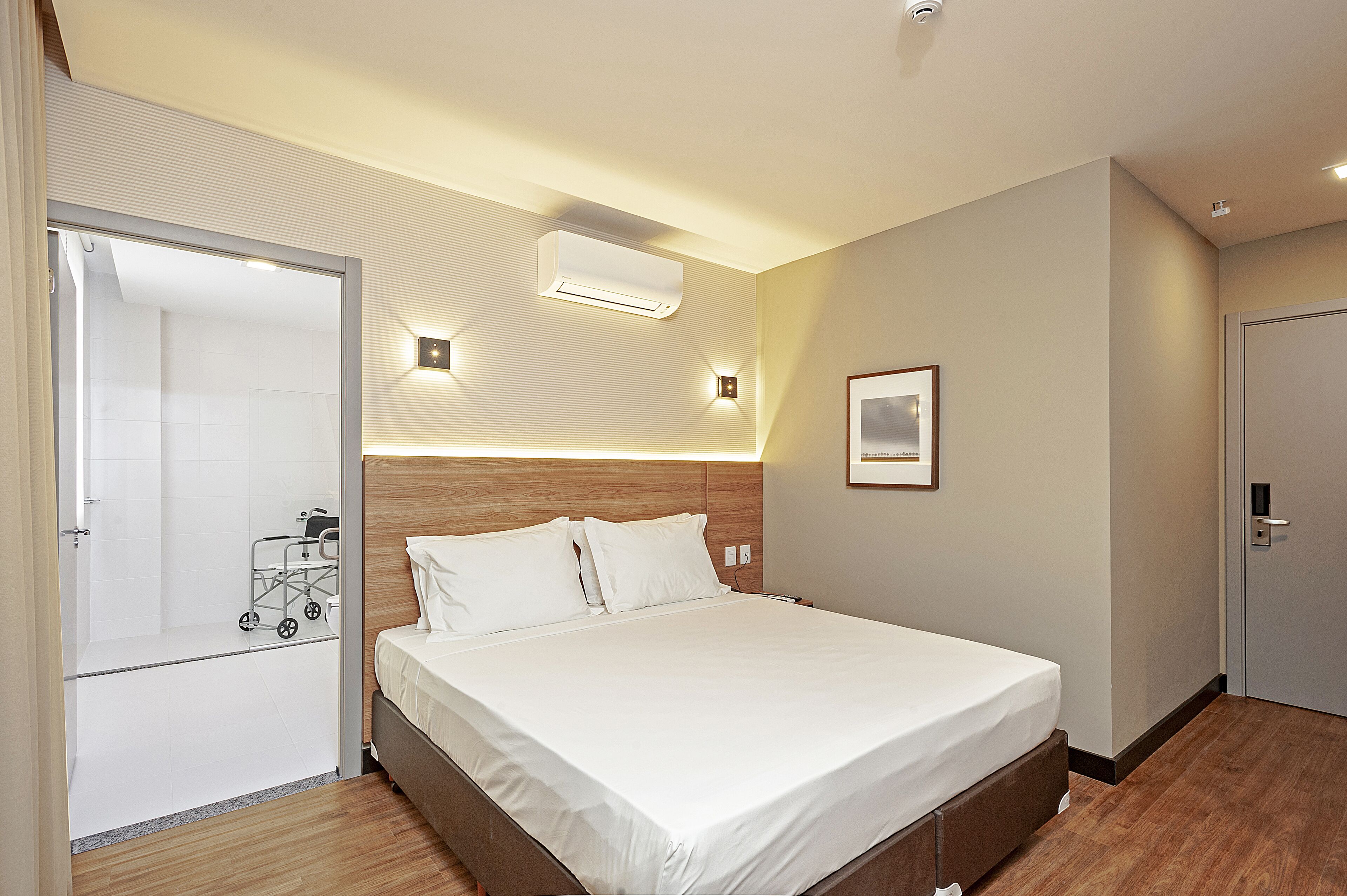Habitación de hotel con cama, mesita de noche, aire acondicionado de pared y una puerta con picaporte.