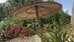 A poolside area with a thatched umbrella, lounge chairs, a decorative wall, and a swimming pool.
