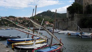 A harbor with several boats docked, a stone building with a tower, and a hillside with buildings in the background.