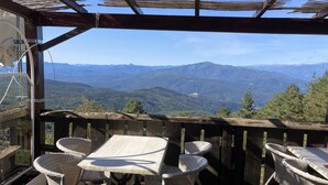 A wooden deck with wicker chairs and a table, overlooking a mountainous landscape.