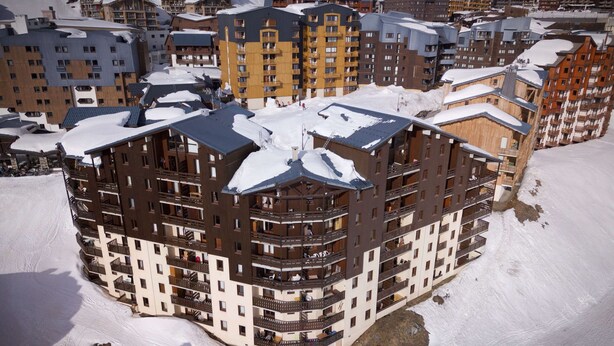 Ein mehrstöckiges Hotel mit Balkonen und einem Ski-Hang im Hintergrund.