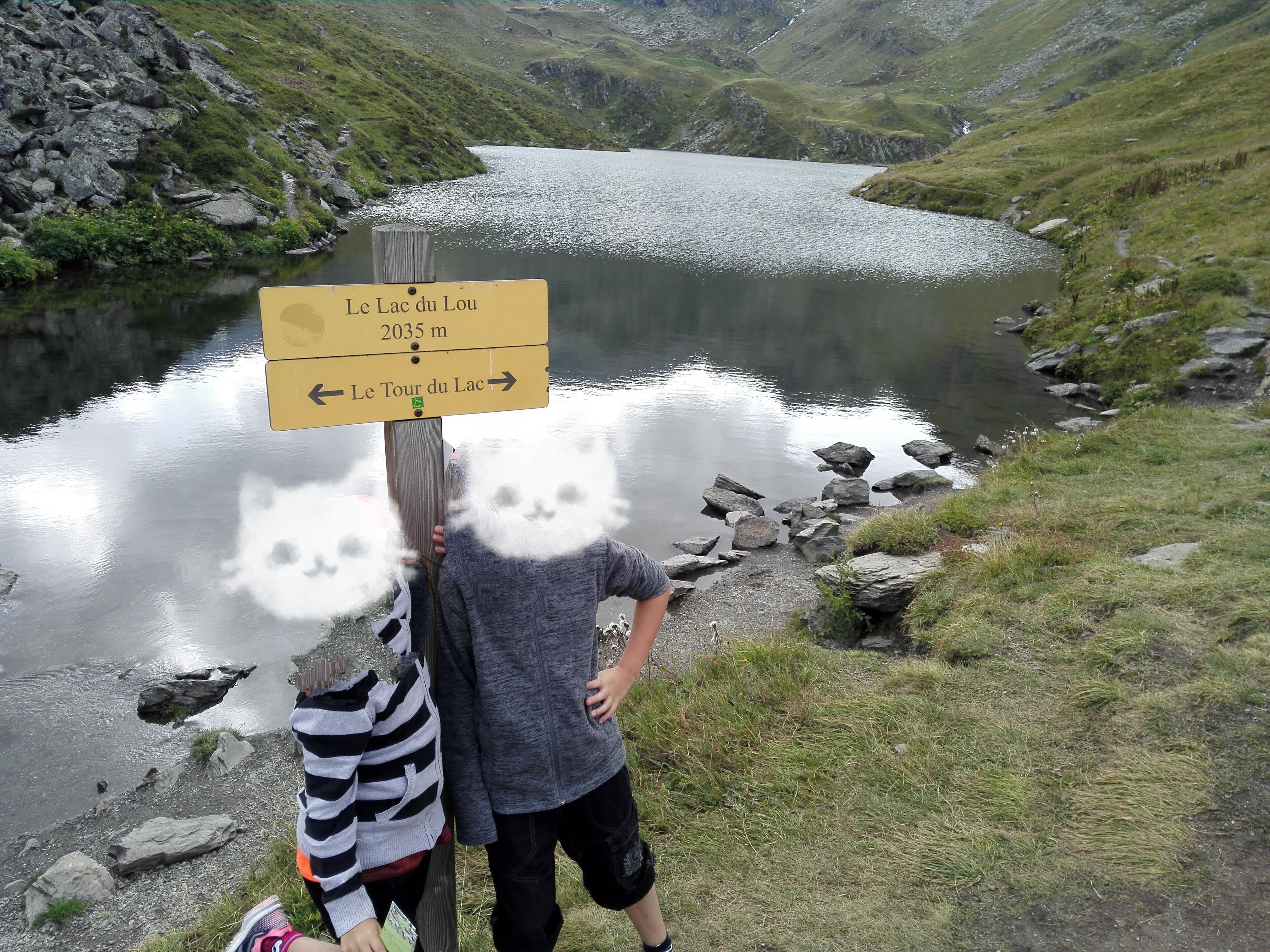 A signpost with directions to 'Le Lac du Lou' and 'Le Tour du Lac' with a mountain backdrop.