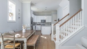 A spacious kitchen with white cabinets, a wooden dining table, and a staircase with white railings. - Luxury Home in Old Town Bluffton + FREE Golf Cart. Sleeps 8 - Downtown location (Bluffton)