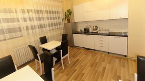 A compact kitchen with white cabinets, a microwave, and a small dining area with a table and chairs. - Moon Hostel (Pristina)