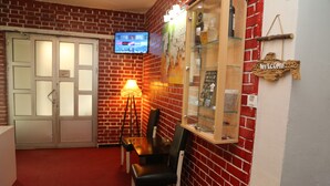 A room with a brick wall, a television mounted on the wall, a wooden cabinet with glass doors, and a 'Welcome' sign. - Moon Hostel (Pristina)